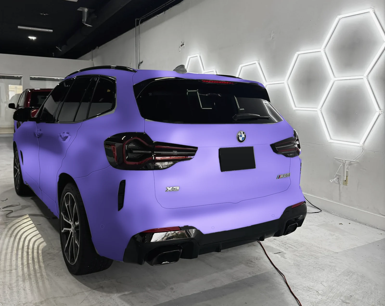 A BMW X3 in our bay under the honeycomb lights, previewed in a purple wrap