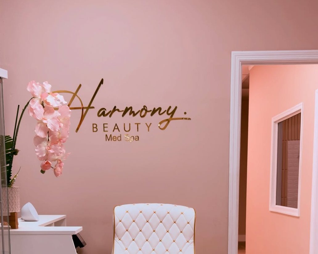 The rose reception at Harmony Beauty Med Spa, the gold Harmony sign on the wall above a white tufted chair