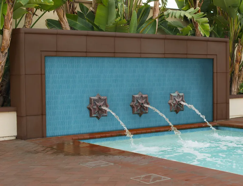 An outdoor blue tiled fountain wall with three bronze spouts