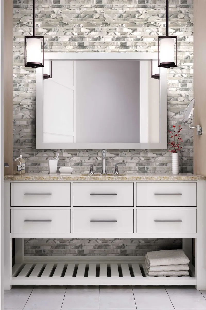 A white bathroom vanity with a grey and cream glass linear mosaic backsplash