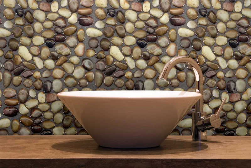 A polished river-pebble mosaic wall behind a white vessel sink