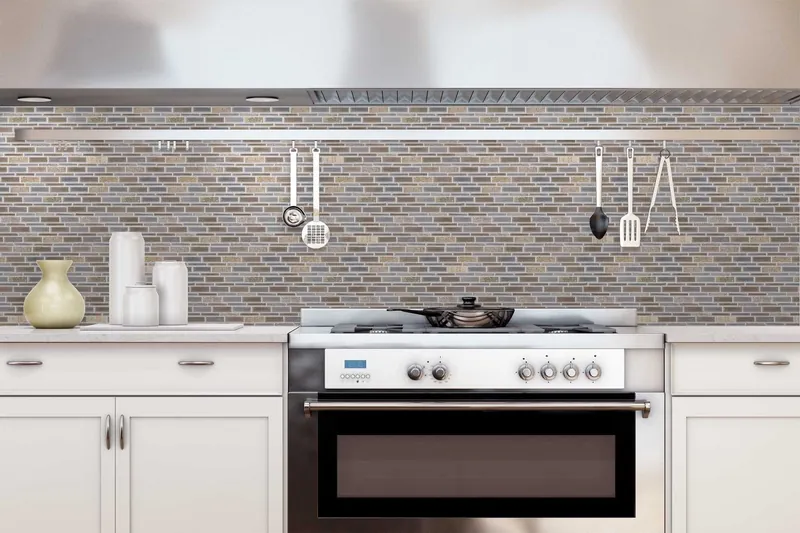 A grey, beige and blue linear glass and stone mosaic backsplash running the full width of a white kitchen