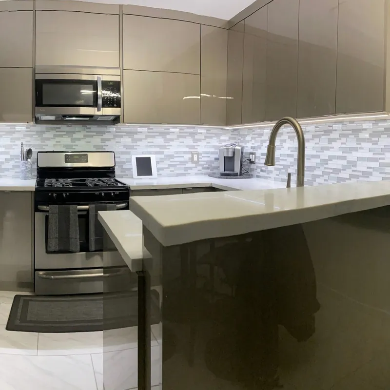 A kitchen with glossy cabinets and a multi-toned glass linear mosaic backsplash
