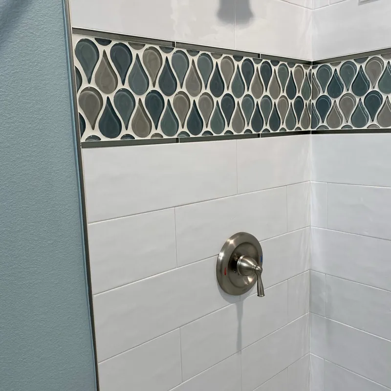 A shower wall in white subway tile with a teardrop glass mosaic border
