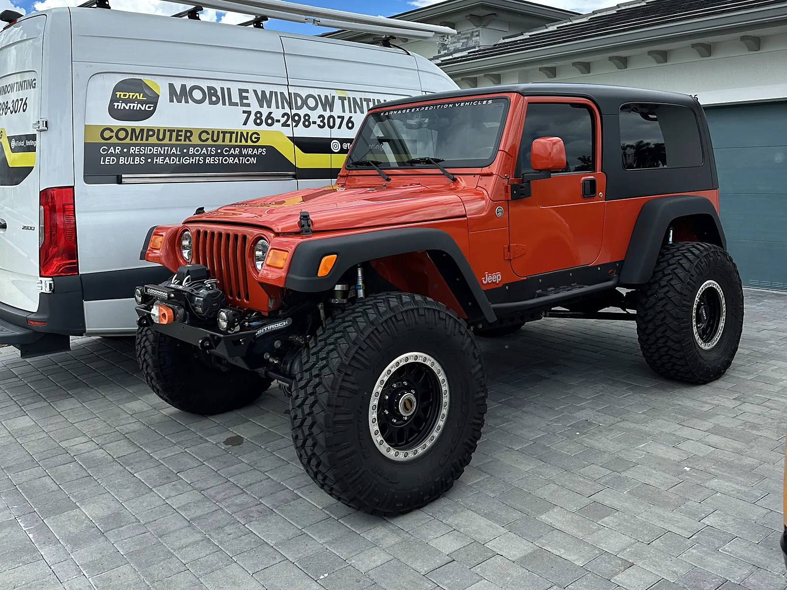 Orange Jeep Wrangler with tinted glass beside the lettered Total Tinting van
